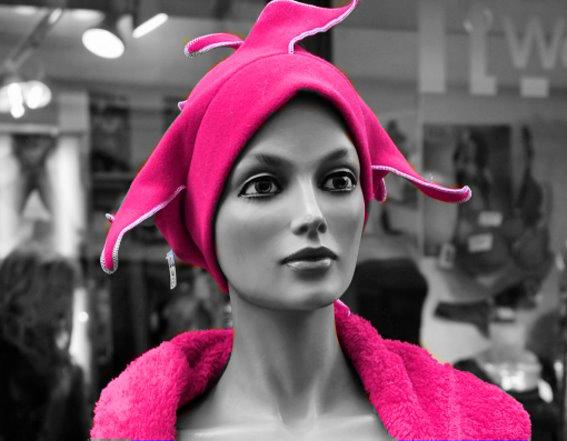 Schwarzweiß-Fotografie einer Schaufensterpuppe mit kräftig pinker Kopfbedeckung und pinkem Oberteil.